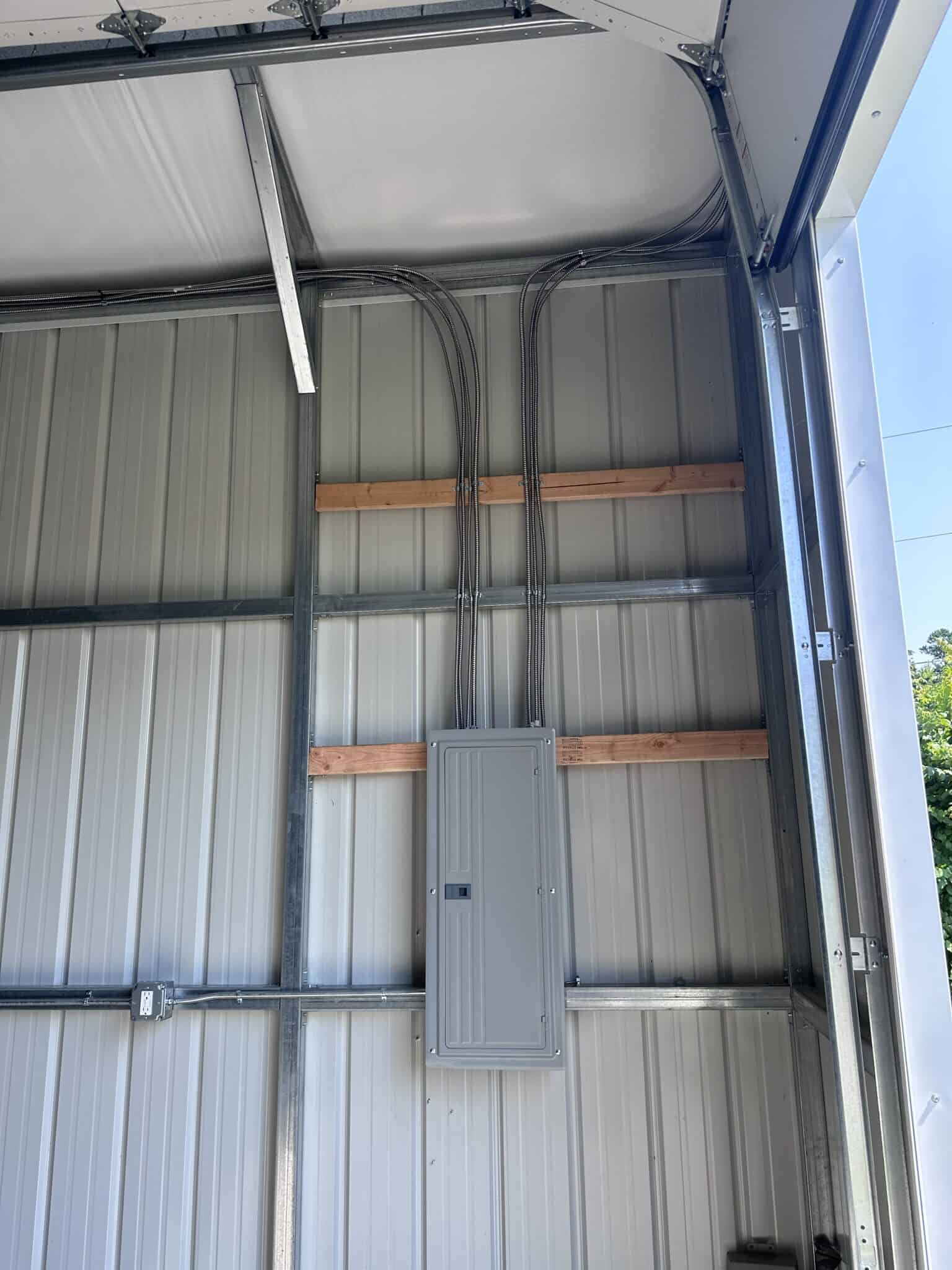 Electrical panel mounted inside a garage wall with conduit wiring.
