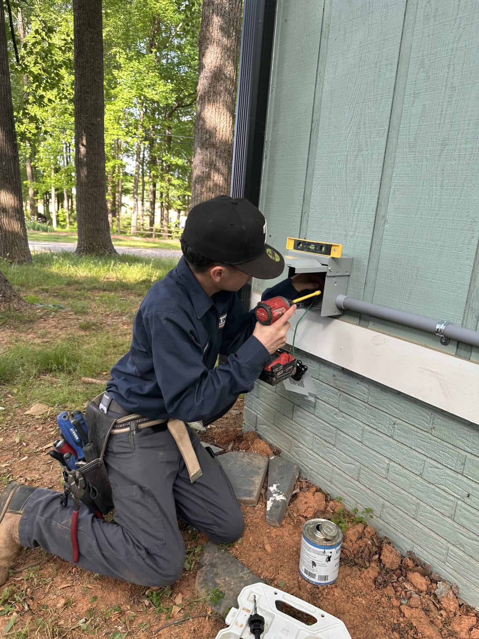 Technician installing outdoor electrical outlet on house exterior for safe power access.