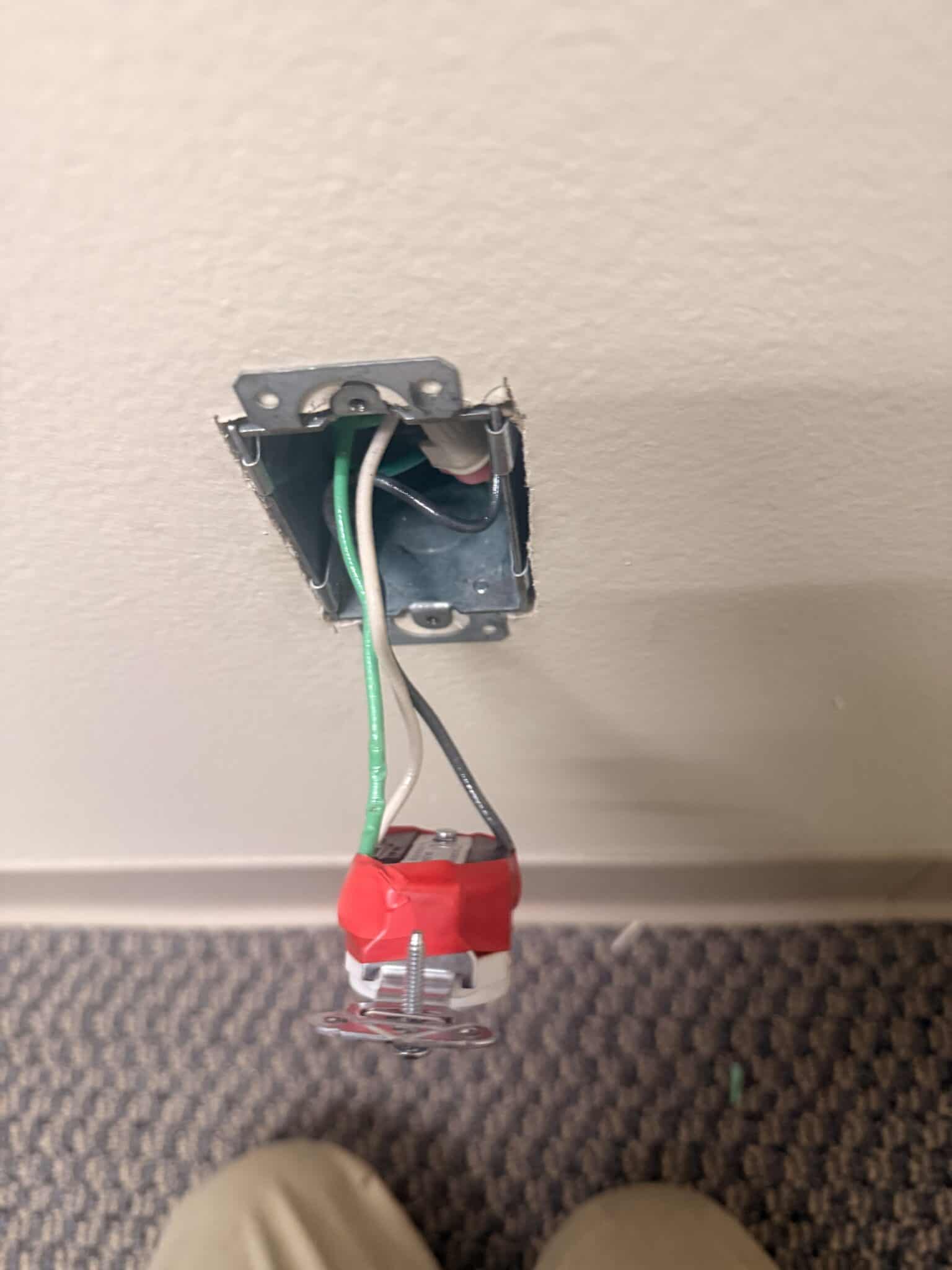 Unfinished electrical outlet wiring in wall with exposed wires.